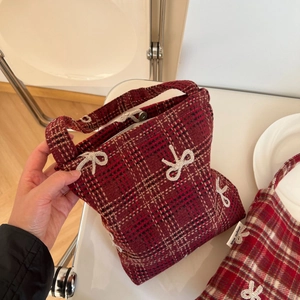 Detail of red plaid wool bag featuring white embroidered bows and silver magnetic clasp
