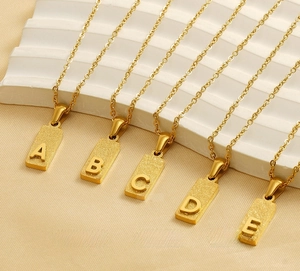 Detail of gold stainless steel A-E block letter pendants with matte and polished texture