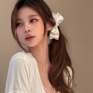 Detail of a white satin polka dot bow hair clip worn elegantly on a low ponytail