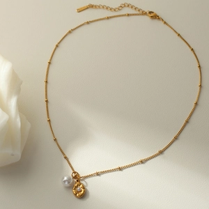 Close-up of gold necklace with shell and pearl pendant on a beige texture surface