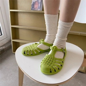 Detail shot of green woven jelly sandals with buckle strap worn with cream textured socks