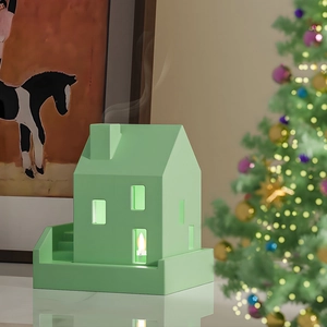 Mint green house-shaped ceramic candle holder with a chimney in a cozy Christmas setting