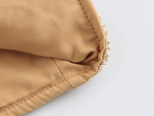 Macro shot of khaki tweed fabric texture and straw fringe tassels on jacket edges