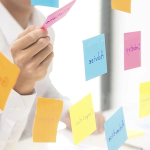 Primer plano de notas adhesivas cuadradas de colores pegadas en una pared de cristal de oficina