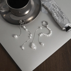 Detailed close-up of asymmetric stainless steel tassel earrings with white pearls