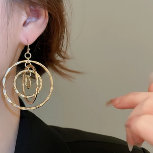 Close-up of golden multi-layered circular earrings with textured metal on a female model