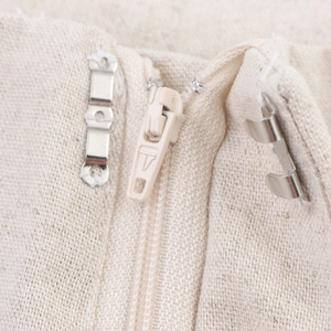 Close-up of beige linen set showing zipper closure and metal hook fastening detail