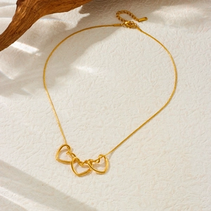 Elegant gold snake chain necklace featuring three interlocking heart pendants on beige surface