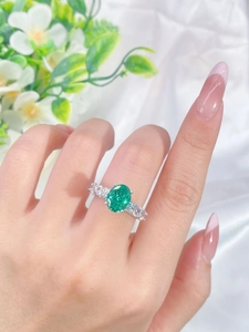 Close-up of S925 silver ring with green emerald-cut stone on hand with silk background