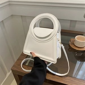 White structured trapezoid handbag with large circular handle and adjustable strap