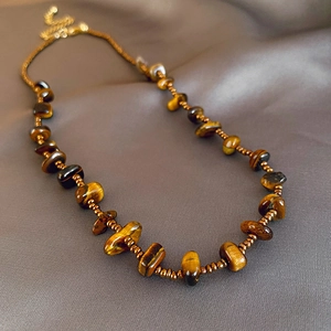 Close-up of irregular tiger eye stone beaded necklace with gold chain on silk fabric