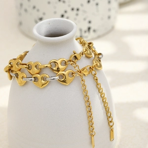 Elegante pulsera de corazón bicolor en oro de 18 quilates y plata sobre un jarrón de cerámica