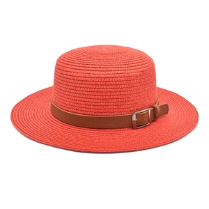 Detalle de sombrero de paja naranja con banda de cuero marrón y hebilla de metal