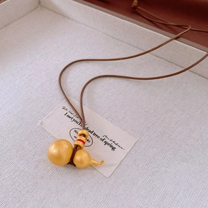 Detail of a matte gold hulu pendant with red bead accents on a brown braided leather cord