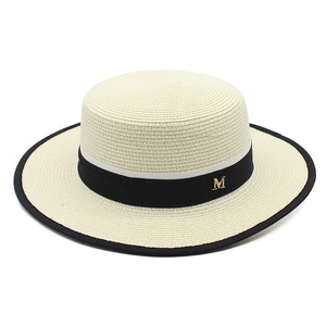 Macro detail of beige woven straw hat with black ribbon and gold M letter decoration