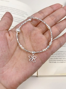 Detail of freshwater pearl bracelet with silver cube beads and flower charm on a hand