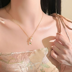 Close-up of golden tulip necklace with pearl pendant on woman's collarbone