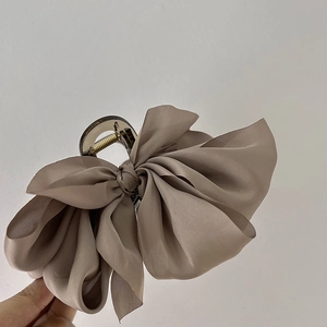 Close-up of a large beige satin bow hair claw clip made of fabric and acrylic resin