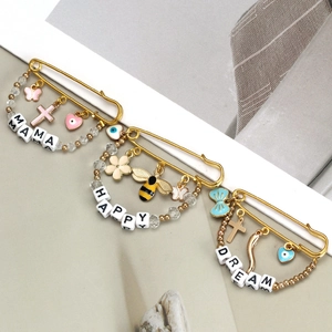 Detailed macro view of gold-tone safety pins with enamel charms and MAMA HAPPY DREAM beads