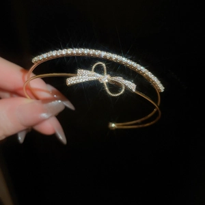 Macro detail of golden double-layer bangle with sparkling pavé bow knot on black background