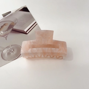 Detail of a pink marble hair claw clip with subtle glitter on a clean white desk