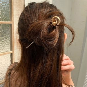 Close-up of a minimalist gold metal hair pin with interlocking rings in a stylish bun