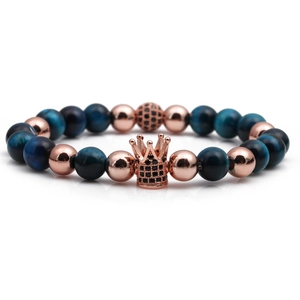 Macro shot of blue tiger eye beads bracelet featuring a rose gold crown charm with black stones