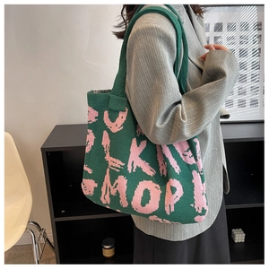 Fashionable green knitted tote bag with pink artistic letters shown on model shoulder