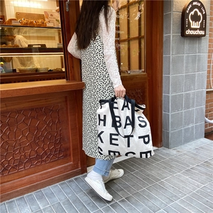 Large capacity canvas tote bag with black logo print shown in street style outdoor scene
