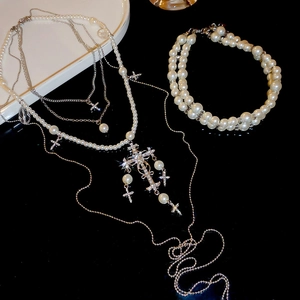 Macro view of crystal cross charms and multi-layer pearl necklace on black surface
