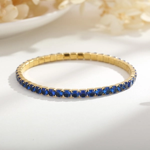 Dettaglio macro del bracciale tennis oro 4mm con cristalli blu su superficie chic