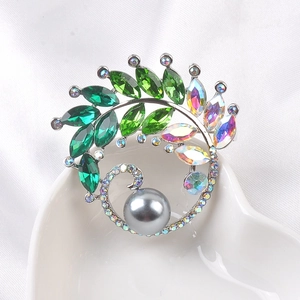 Detailed close-up of a luxury green crystal brooch with a large grey pearl on a ceramic tray