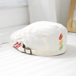 Close-up of white cotton beret featuring red letter embroidery and paperclip detail
