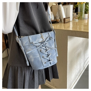 Détail du sac seau en denim bleu clair avec laçage style corset et oillets métalliques