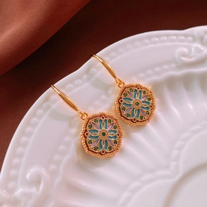 Macro detail of vintage floral enamel earrings with gold plating on a white ceramic plate