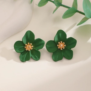 Macro shot of dark green flower earrings with golden stamens on a white textured surface