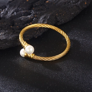 Twisted cable cuff bracelet in gold finish with two white pearls on black stone background