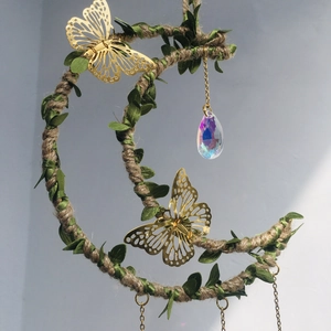 Detail of moon-shaped wind chime with hemp rope, green leaves, and crystal pendant