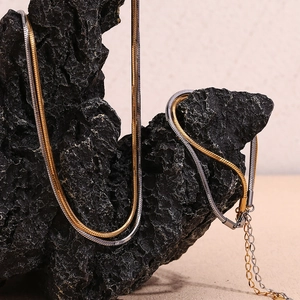 Close-up of two-tone flat snake chain in gold and silver on black volcanic rock base