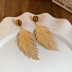 Detail of leaf-shaped gold stud earring with tiger eye stone on ceramic tray