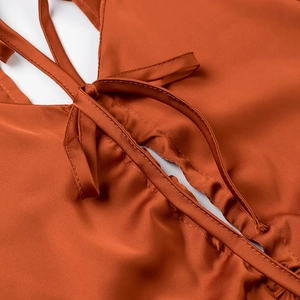 Détail d'un crop top en satin marron rouille avec découpe et nœud papillon à l'avant