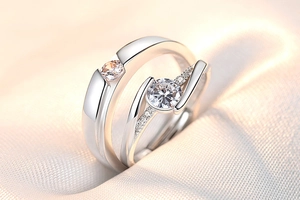 Macro shot of silver crown couple rings with sparkling zircon stones on soft silk fabric