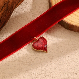 Dettaglio di un choker in velluto rosso con un ciondolo a cuore dorato scintillante