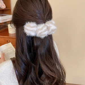 Détail d'une pince à cheveux à pompons en fausse fourrure crème sur cheveux ondulés