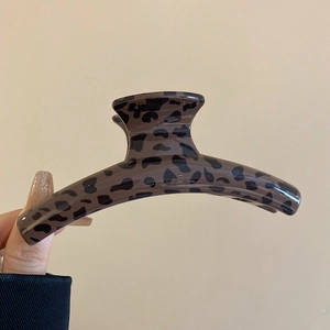Close-up of a large leopard print hair claw clip held by hand against a beige background