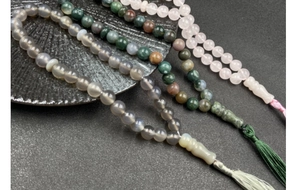 Macro shot of natural crystal prayer beads in grey-blue, green, and pink with tassel detail