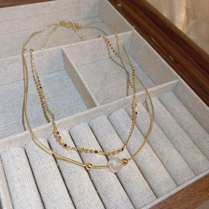 Detail view of double-layered gold necklace with iridescent pearl charm in a wooden box