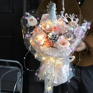 Christmas bouquet with roses, pinecones, elf doll and LED lights in snowflake wrapping