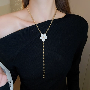 Detail of elegant gold beaded Y-shaped necklace with white flower pendant on model