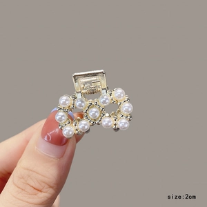 Detail view of a 2cm golden metal hair claw clip featuring pearls in a bow shape